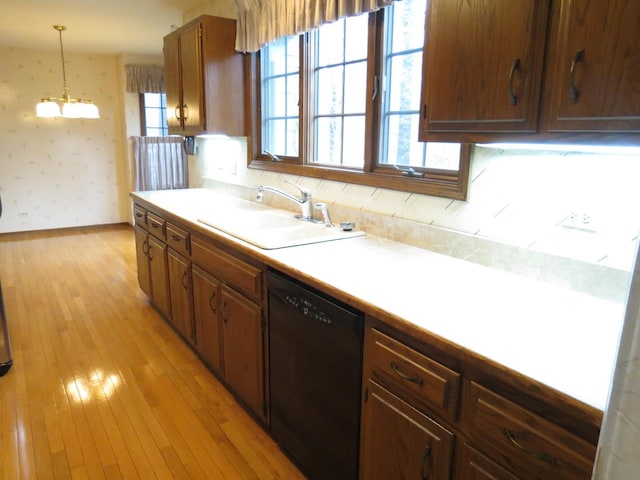 kitchen with black dishwasher, light countertops, light wood-style floors, a sink, and wallpapered walls