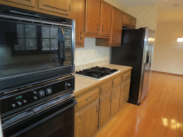 kitchen featuring light wood finished floors, wallpapered walls, brown cabinetry, light countertops, and black appliances