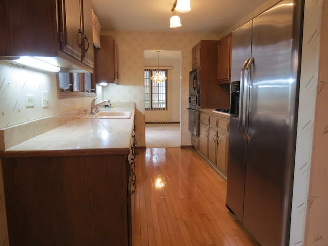 kitchen with light wood-style flooring, a sink, light countertops, black appliances, and wallpapered walls