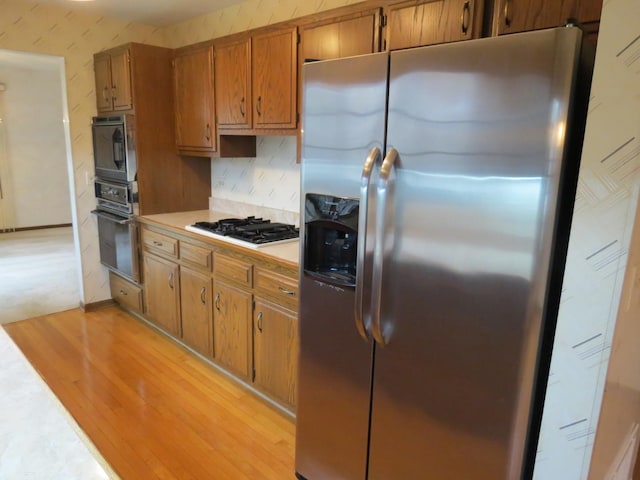 kitchen featuring gas stovetop, black oven, built in microwave, light wood finished floors, and stainless steel fridge