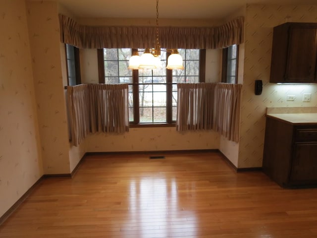 unfurnished dining area with light wood-style floors and wallpapered walls