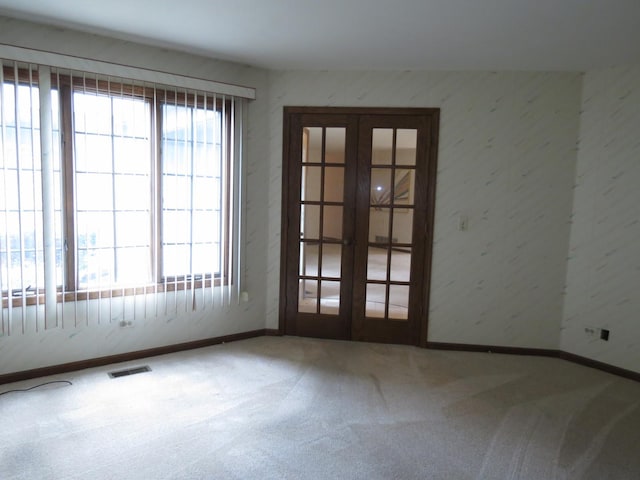 empty room featuring french doors, visible vents, plenty of natural light, and carpet flooring