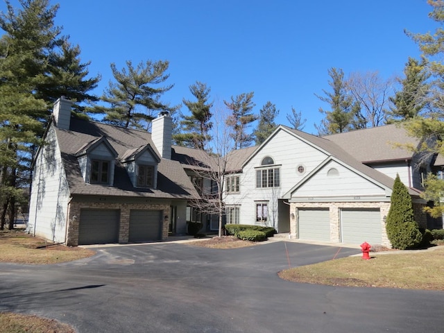 view of front of home featuring aphalt driveway, brick siding, a chimney, a shingled roof, and an attached garage