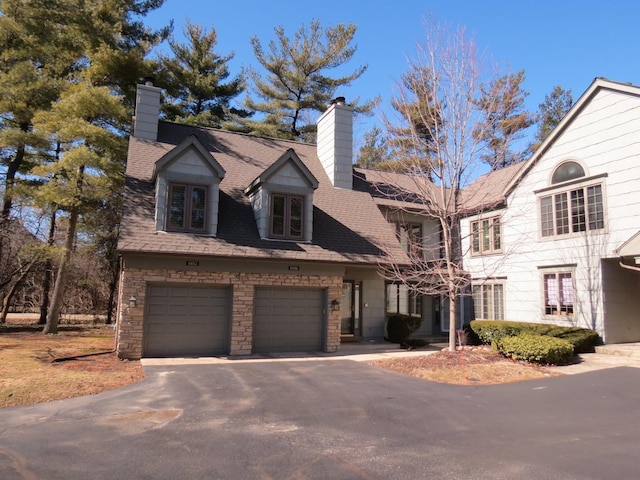 view of front of home with a garage, driveway, a chimney, and roof with shingles