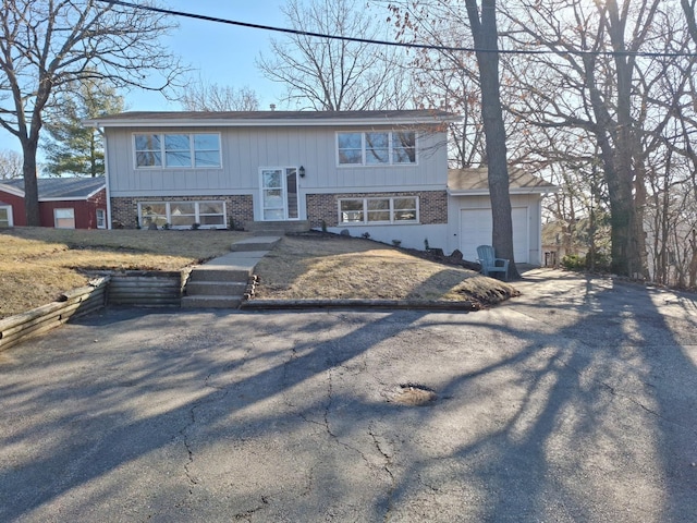 raised ranch featuring brick siding, aphalt driveway, and a garage