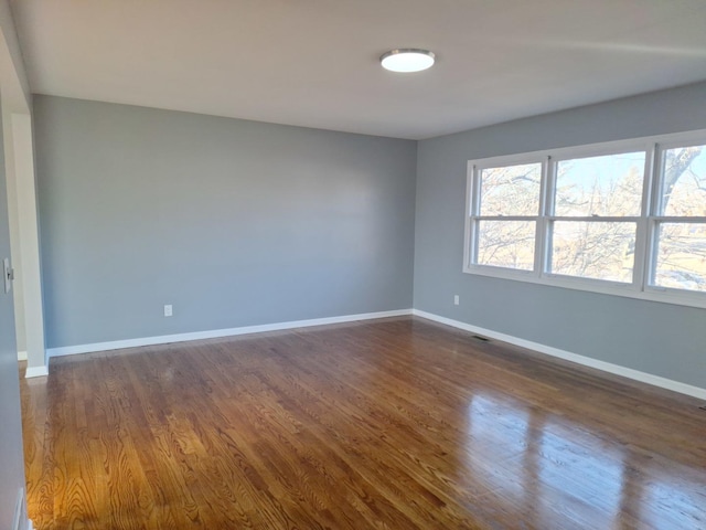 empty room with baseboards, a healthy amount of sunlight, and dark wood finished floors