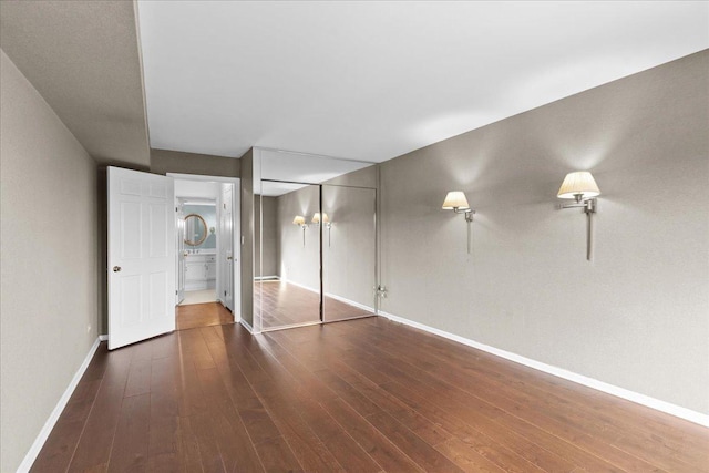 unfurnished bedroom featuring wood-type flooring, baseboards, a closet, and ensuite bathroom