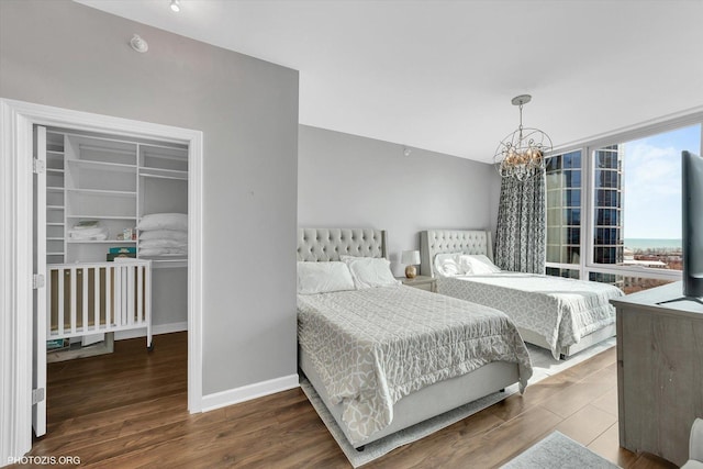 bedroom featuring wood finished floors, baseboards, floor to ceiling windows, a walk in closet, and a chandelier