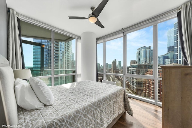 bedroom with a city view, floor to ceiling windows, ceiling fan, and wood finished floors