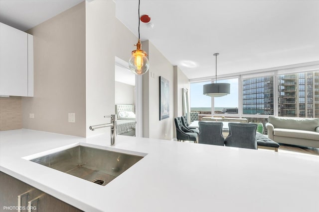 kitchen with a sink, white cabinets, light countertops, decorative backsplash, and hanging light fixtures