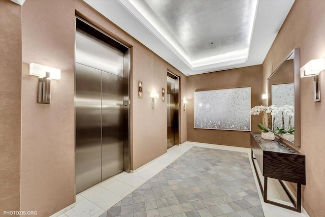 hallway featuring a tray ceiling, elevator, and baseboards