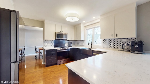 kitchen with appliances with stainless steel finishes, decorative backsplash, a sink, and light wood-style floors