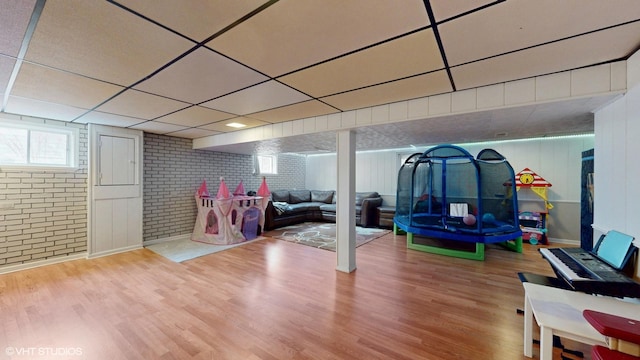 playroom with brick wall, a drop ceiling, and wood finished floors