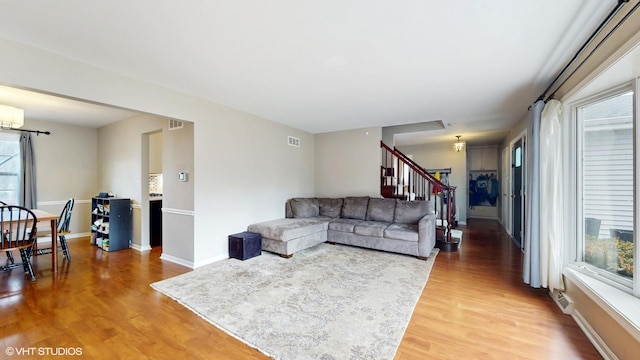 living room featuring light wood-style flooring, stairs, visible vents, and baseboards