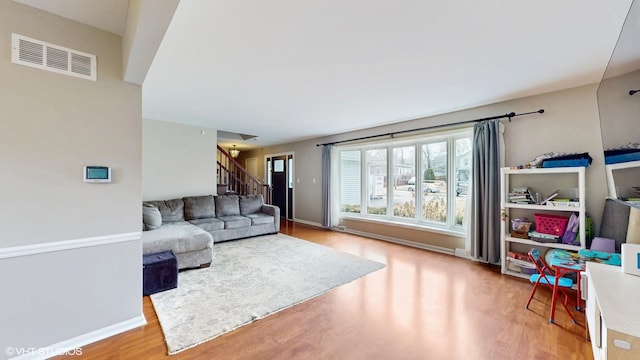 living room featuring stairway, wood finished floors, visible vents, and baseboards