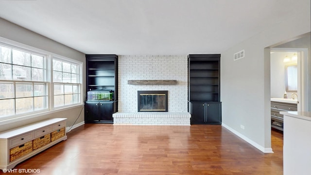 unfurnished living room with built in features, visible vents, a brick fireplace, wood finished floors, and baseboards