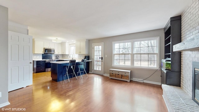 kitchen featuring a breakfast bar, appliances with stainless steel finishes, light wood-type flooring, backsplash, and a brick fireplace