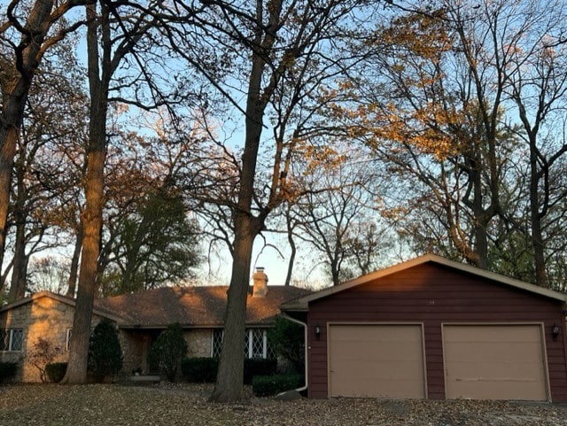 ranch-style house with a garage, stone siding, and a chimney