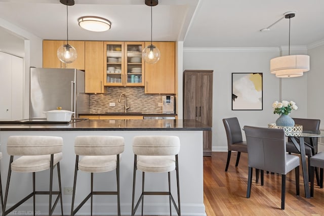 kitchen with wood finished floors, freestanding refrigerator, a sink, a kitchen bar, and backsplash