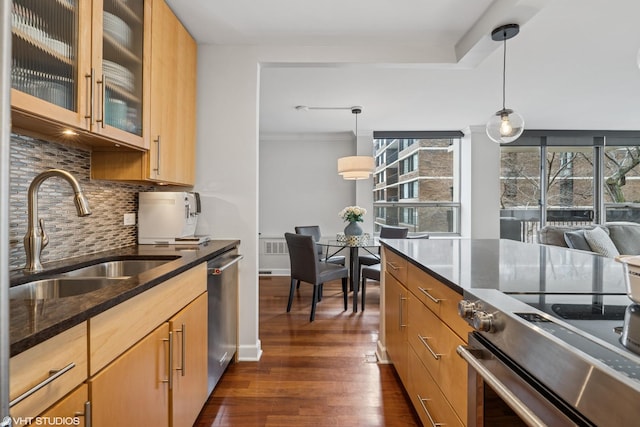 kitchen featuring dark wood finished floors, dark stone counters, decorative light fixtures, stainless steel appliances, and a sink