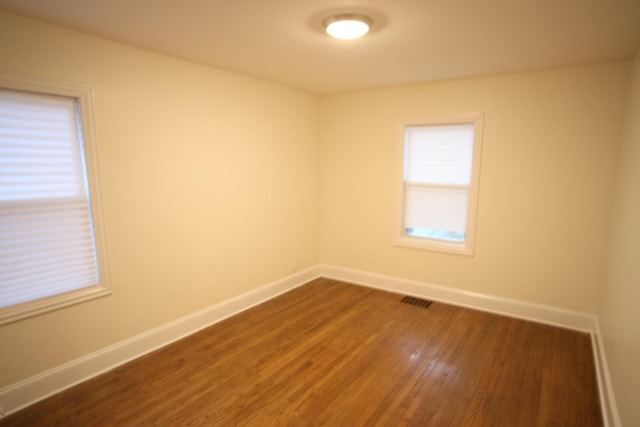 spare room featuring dark wood-style floors, plenty of natural light, visible vents, and baseboards