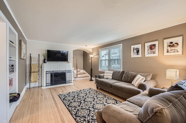 living room with arched walkways, light wood finished floors, stairway, a fireplace with flush hearth, and baseboards