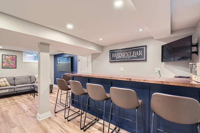 bar with light wood-style floors, recessed lighting, bar area, and baseboards