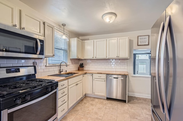 kitchen featuring butcher block countertops, appliances with stainless steel finishes, backsplash, a sink, and light tile patterned flooring