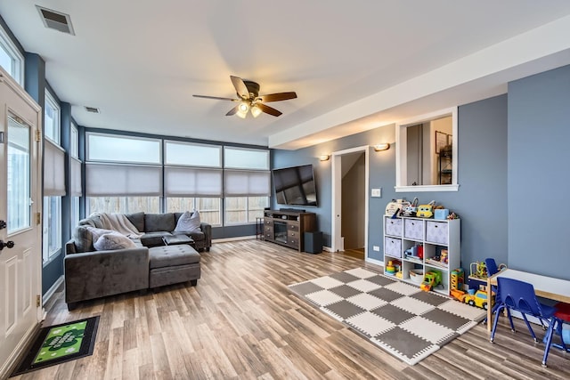 living room with baseboards, wood finished floors, visible vents, and a ceiling fan