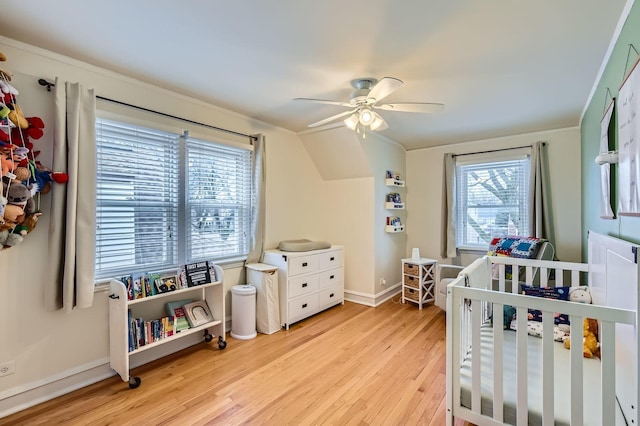 bedroom featuring a crib, light wood-style flooring, baseboards, and a ceiling fan