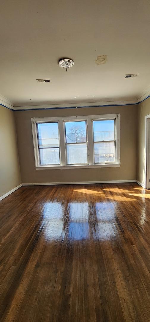 unfurnished room with a wealth of natural light, wood-type flooring, visible vents, and baseboards