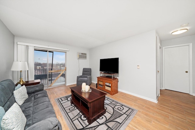 living room featuring a wall mounted air conditioner, baseboards, and light wood finished floors