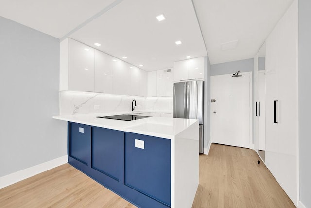 kitchen with a peninsula, light wood-style floors, white cabinets, freestanding refrigerator, and modern cabinets