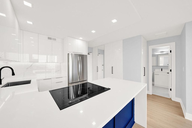 kitchen with black electric stovetop, freestanding refrigerator, white cabinetry, a sink, and modern cabinets