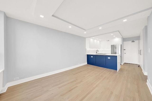 kitchen with a peninsula, a sink, white cabinetry, light wood-style floors, and light countertops