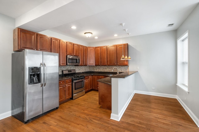 kitchen featuring stainless steel appliances, a peninsula, a sink, visible vents, and tasteful backsplash