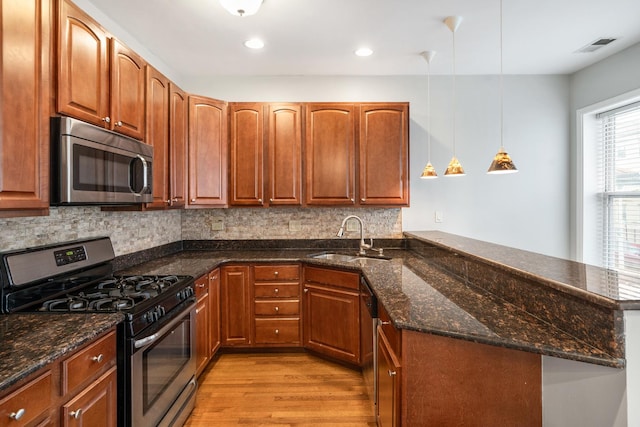 kitchen featuring a peninsula, a sink, stainless steel appliances, light wood-style floors, and backsplash