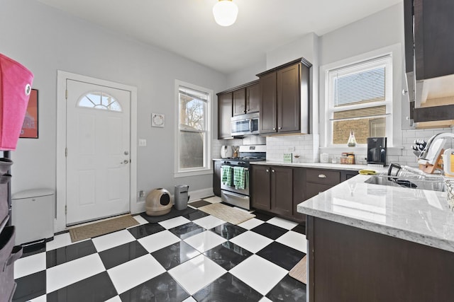 kitchen featuring dark brown cabinetry, tasteful backsplash, stainless steel appliances, light floors, and a sink