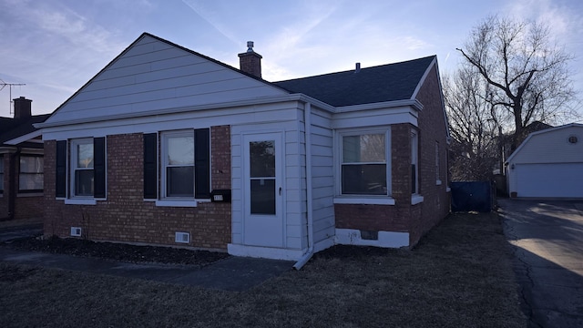 view of front of home featuring a shingled roof, a chimney, an outdoor structure, crawl space, and brick siding