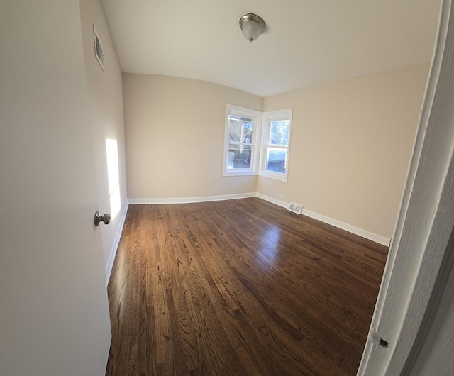 unfurnished room with dark wood-type flooring, visible vents, and baseboards