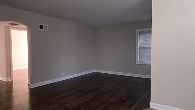 unfurnished room featuring dark wood-type flooring, arched walkways, visible vents, and baseboards