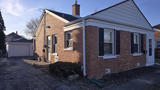 view of side of property with brick siding, a detached garage, a chimney, an outdoor structure, and driveway