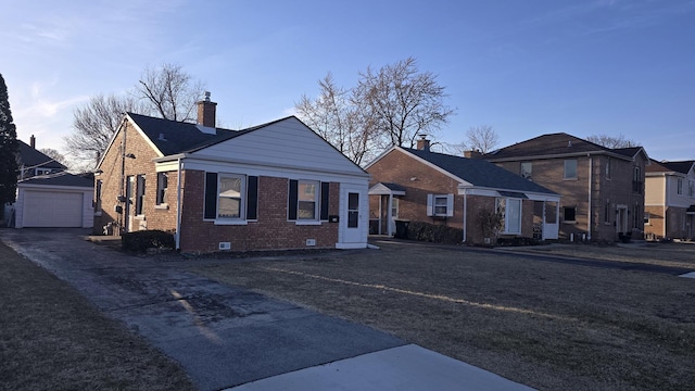 bungalow-style home with brick siding, a chimney, a garage, an outbuilding, and driveway