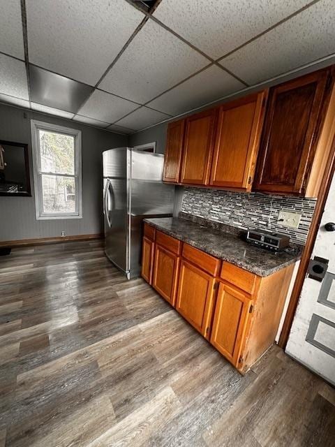 kitchen with dark wood finished floors, brown cabinetry, freestanding refrigerator, and decorative backsplash