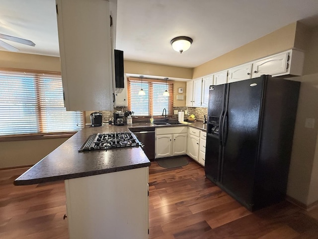 kitchen featuring dark countertops, black refrigerator with ice dispenser, stainless steel dishwasher, white cabinets, and stovetop