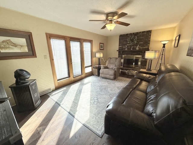 living room featuring a textured ceiling, ceiling fan, a fireplace, and wood finished floors