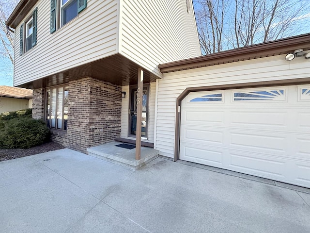 doorway to property featuring a garage, concrete driveway, and brick siding