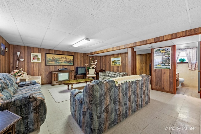 living room with light floors, wooden walls, and a drop ceiling