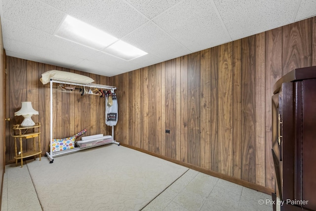 unfurnished room featuring baseboards, a paneled ceiling, and wooden walls