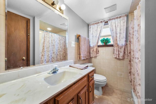 bathroom with visible vents, toilet, tile patterned flooring, vanity, and tile walls